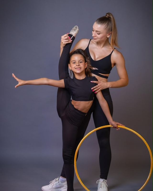 A coach guiding a young gymnast through a hoop exercise in the studio