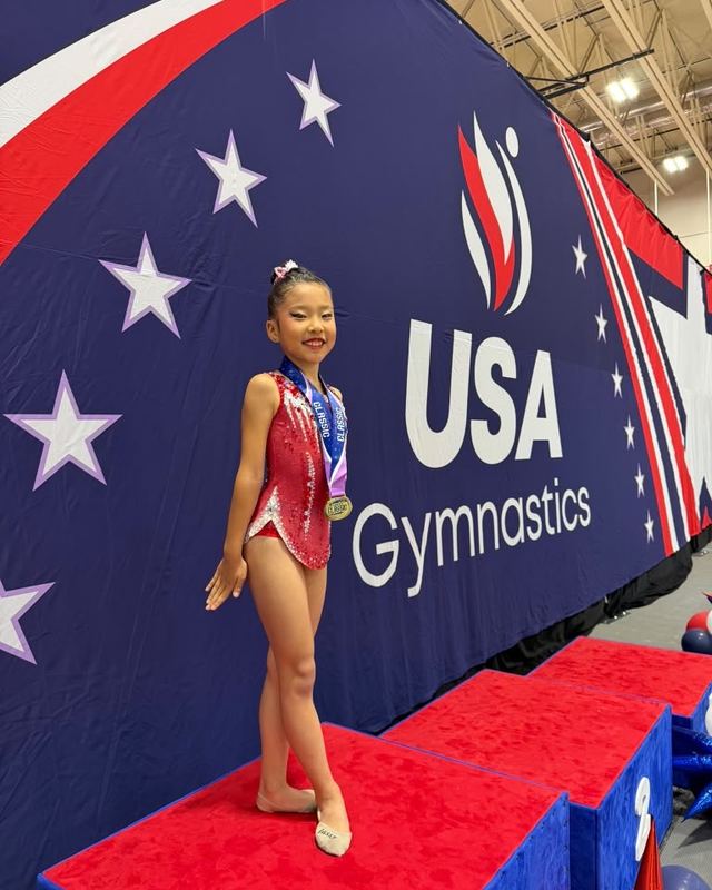 A gymnast standing in front of the USA Gymnastics backdrop