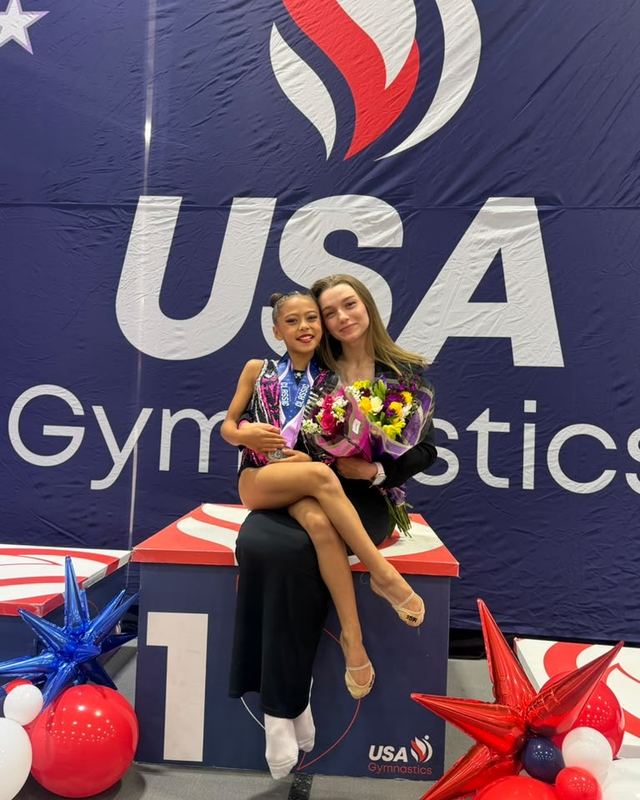 Two gymnasts on the top step of a USA Gymnastics podium with flowers