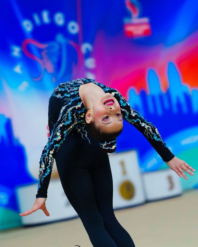 A gymnast in a deep backbend against a bright competition backdrop
