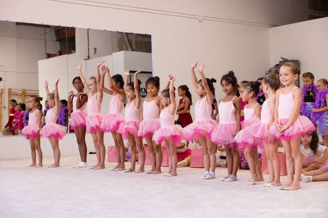 A long line of the youngest gymnasts in pink tutus with their arms raised
